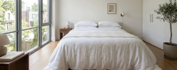 Chambre contemporaine lumineuse avec lit double parfaitement fait, couette blanche à la retombée généreuse tombant harmonieusement sur les côtés